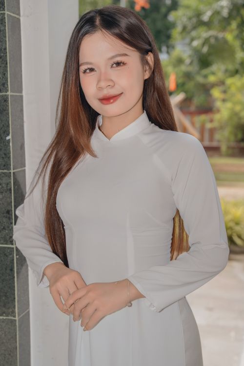 Free A young woman in a white Ao Dai dress posing outside, showcasing traditional Vietnamese attire. Stock Photo