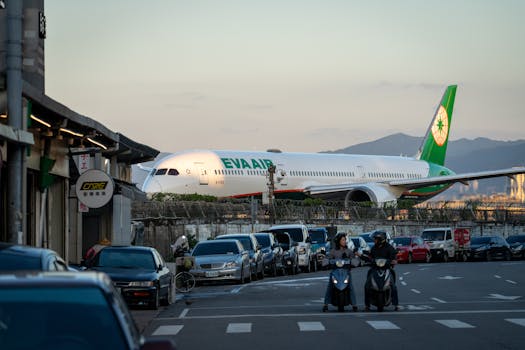 EVA Airplane taxiing near urban street during sunset with vehicles and people nearby.