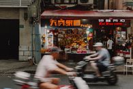 一张动态图像中，摩托车手正经过上海街道上一个充满活力的水果摊