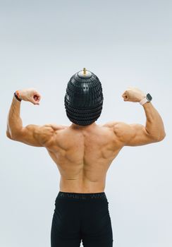 Back view of a muscular man flexing in gym gear, wearing a distinctive helmet.