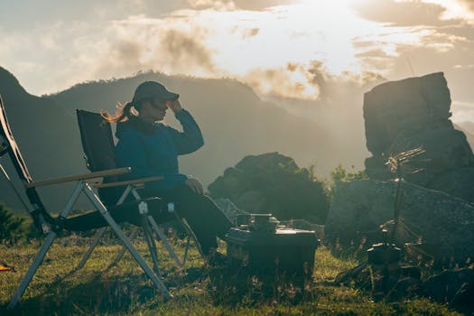 Serene camping scene with woman relaxing near campfire as sun rises over mountains.