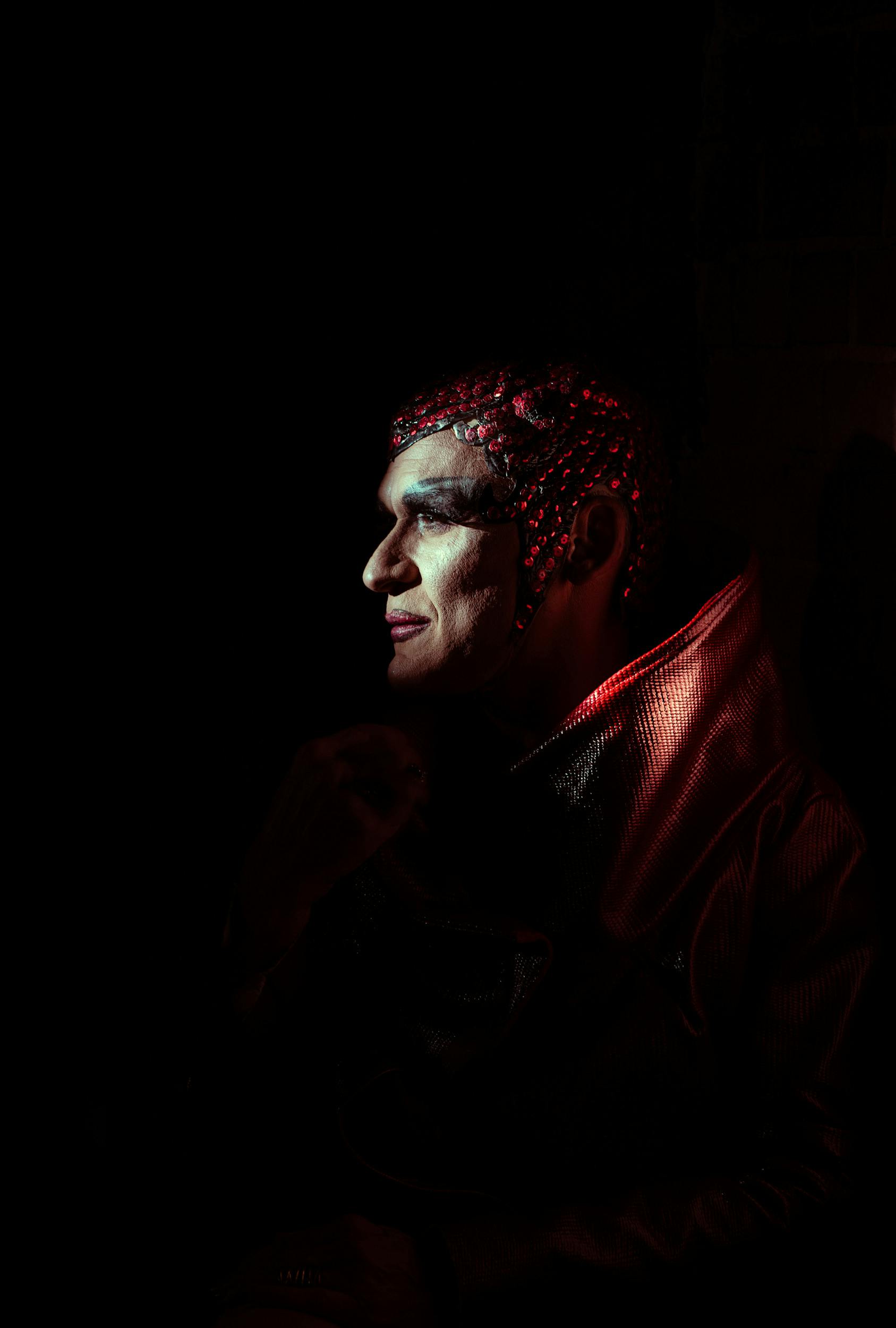 Profile portrait of a person in costume with dramatic red lighting.