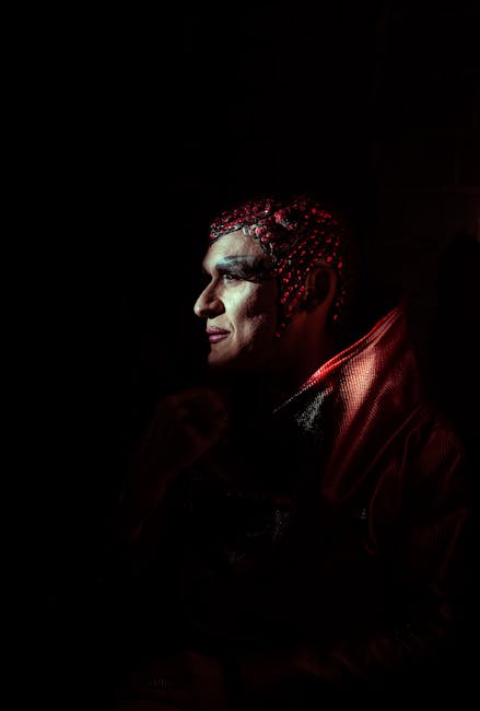 Profile portrait of a person in costume with dramatic red lighting.