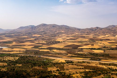 Free A breathtaking aerial shot showcasing patchwork farmland with rolling mountains in the background under a clear blue sky. Stock Photo