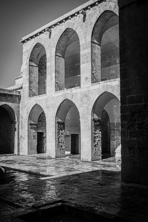 Free Black and white photo of a historic stone courtyard featuring arches and strong shadows, capturing timeless architecture. Stock Photo