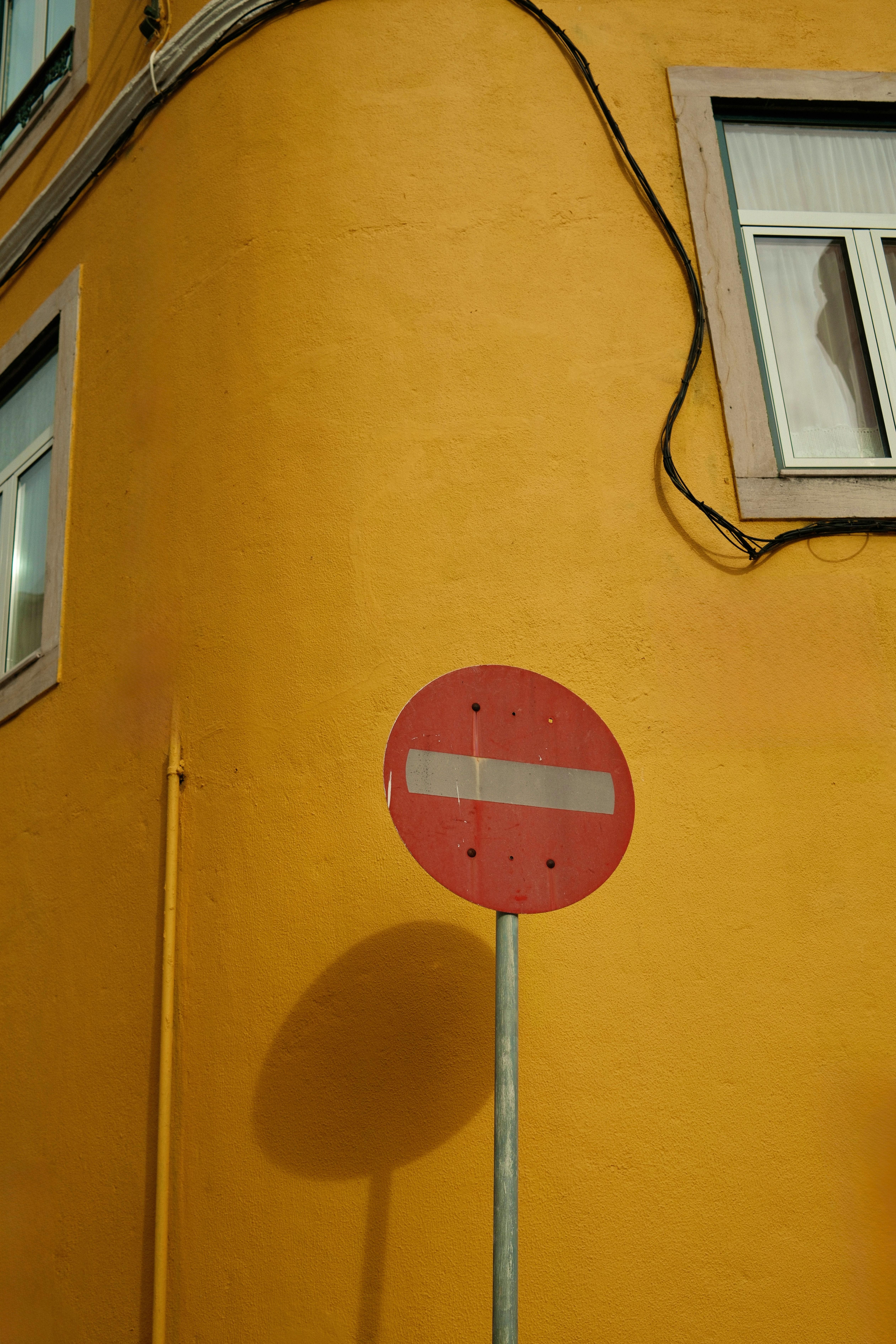 Gratis Una señal roja de prohibido el paso contra una pared de un edificio de color amarillo brillante en Lisboa, Portugal. Foto de stock