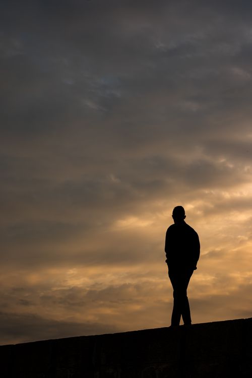 Free A lone silhouette of a person standing against a dramatic sunset sky, evoking solitude and reflection. Stock Photo