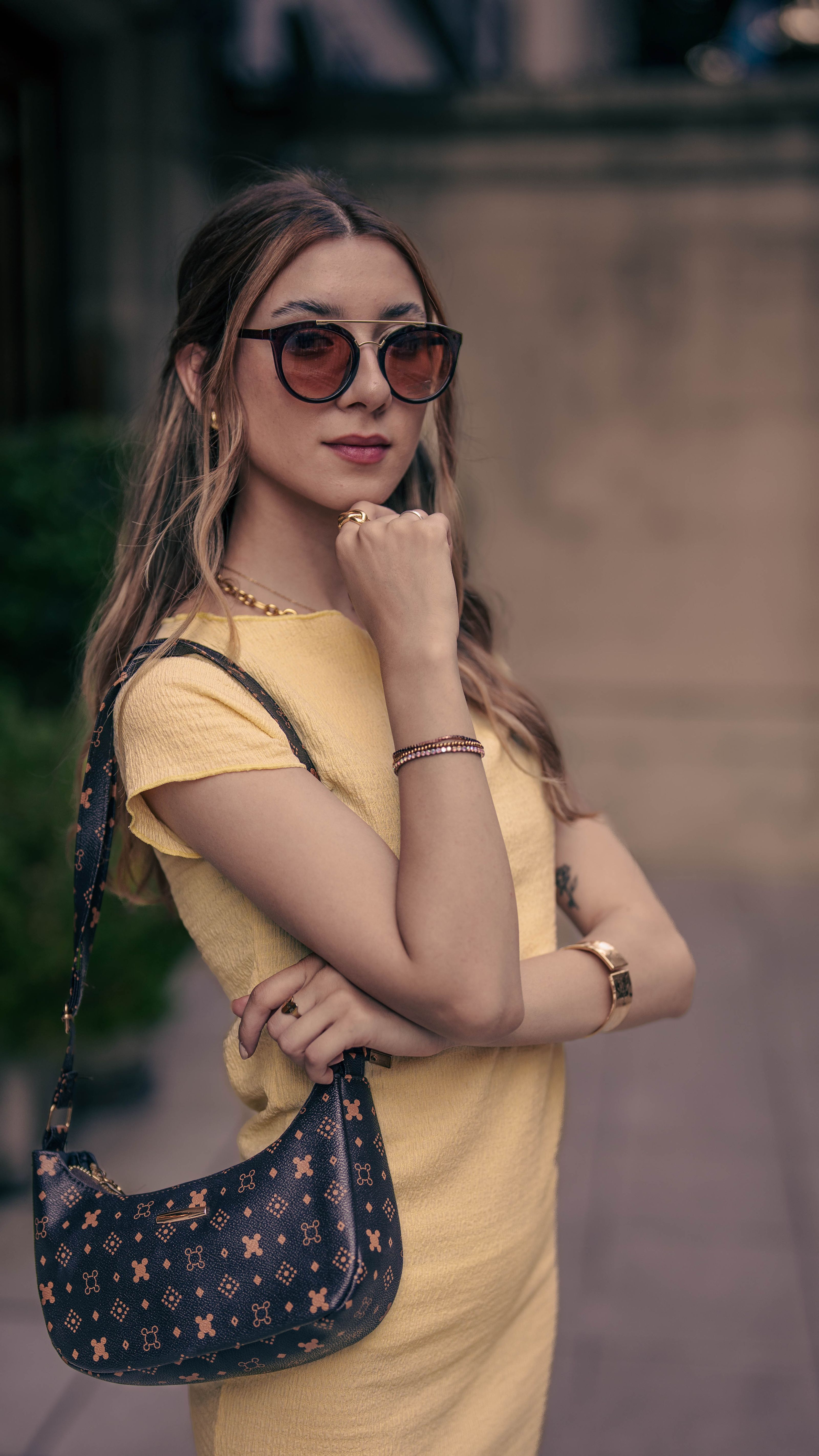Mulher elegante de vestido amarelo e óculos de sol posando ao ar livre com confiança e estilo.