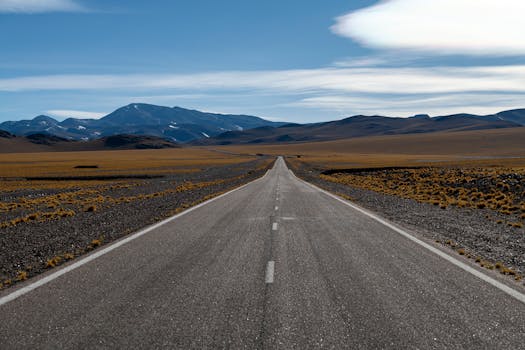 A wide, open highway stretches towards distant mountains under a clear blue sky.
