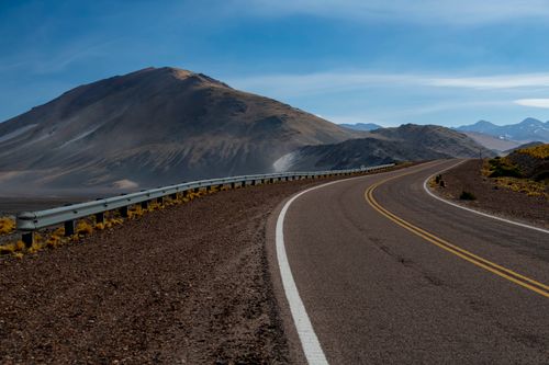 Free A scenic mountain road curves through a barren landscape under a clear blue sky. Stock Photo