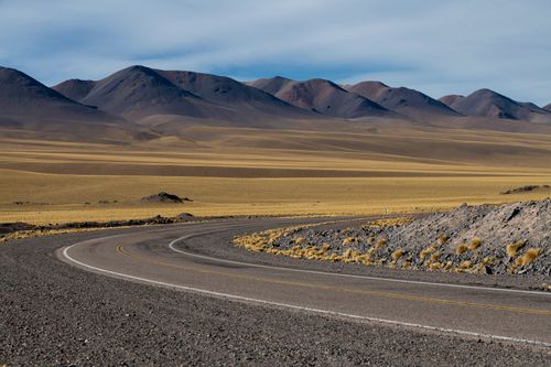 Free A winding road curves through a vast desert landscape with mountain background. Stock Photo
