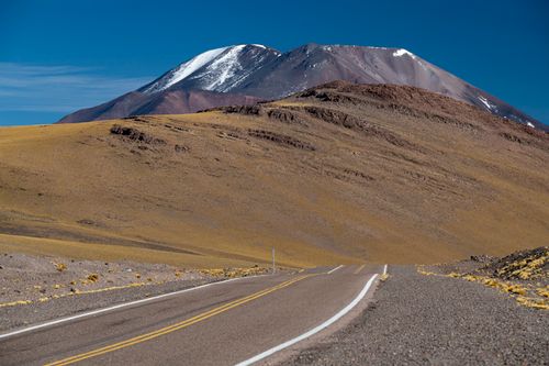 Free Desolate road leading to snow-capped mountains under clear blue skies. Stock Photo