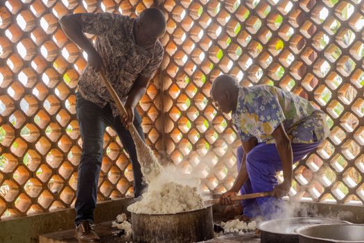 Two men cooking traditional African fufu in a kitchen with brick lattice walls.