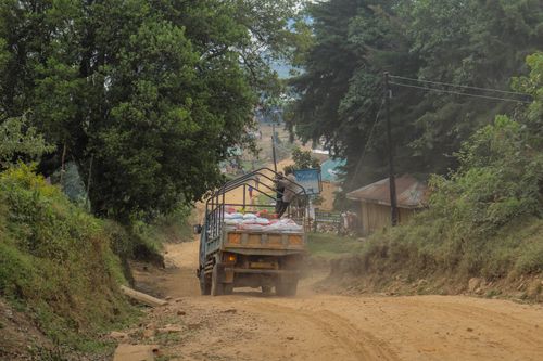 Free A truck navigates a rural dirt road in a verdant countryside setting with lush trees. Stock Photo