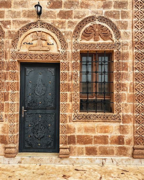 Free Beautifully crafted stone facade with an ornate black door and window, showcasing detailed carvings. Stock Photo