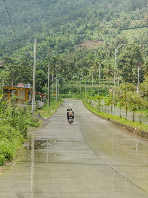 Free A motorcyclist rides on a wet road surrounded by lush green hills in Jawa Barat, Indonesia. Stock Photo