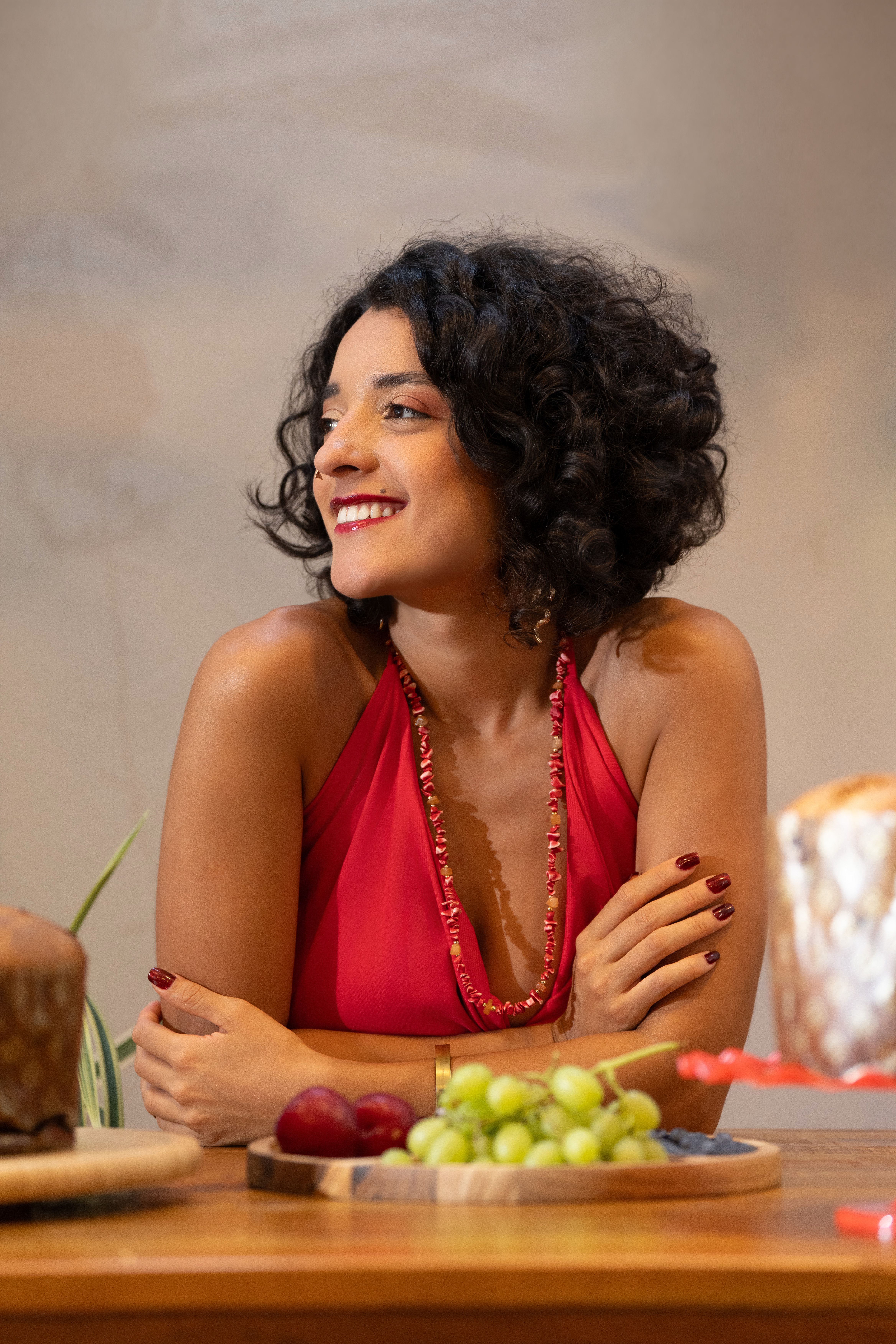 Happy woman in a red dress sitting at a table with fruits indoors.