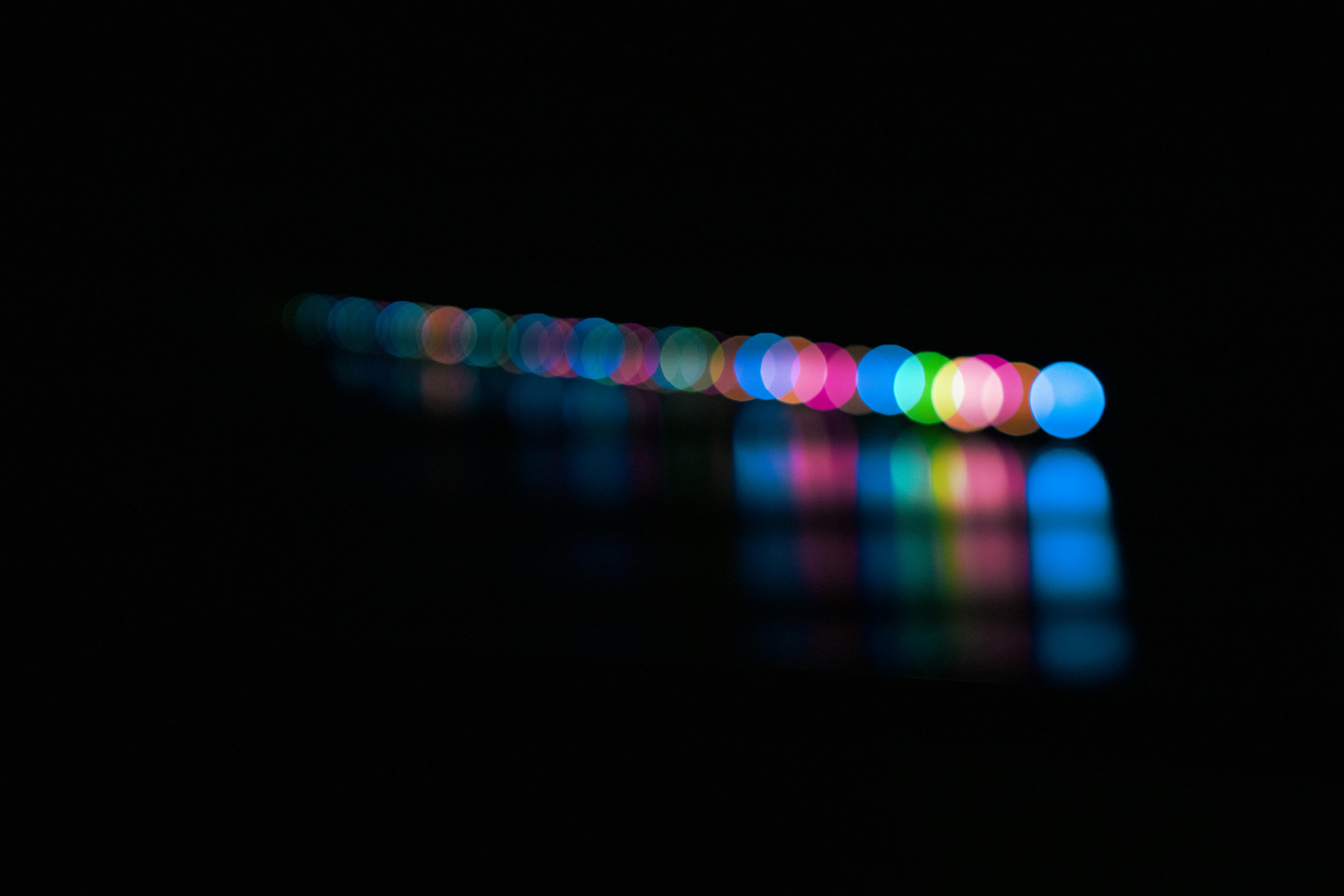 grátis Esferas de bokeh coloridas em linha, criando um padrão abstrato vibrante contra um fundo escuro. Foto profissional