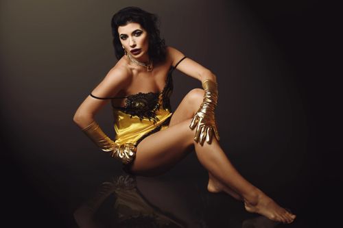 Free An elegant woman in a glamorous gold dress with matching gloves posed artistically. Stock Photo