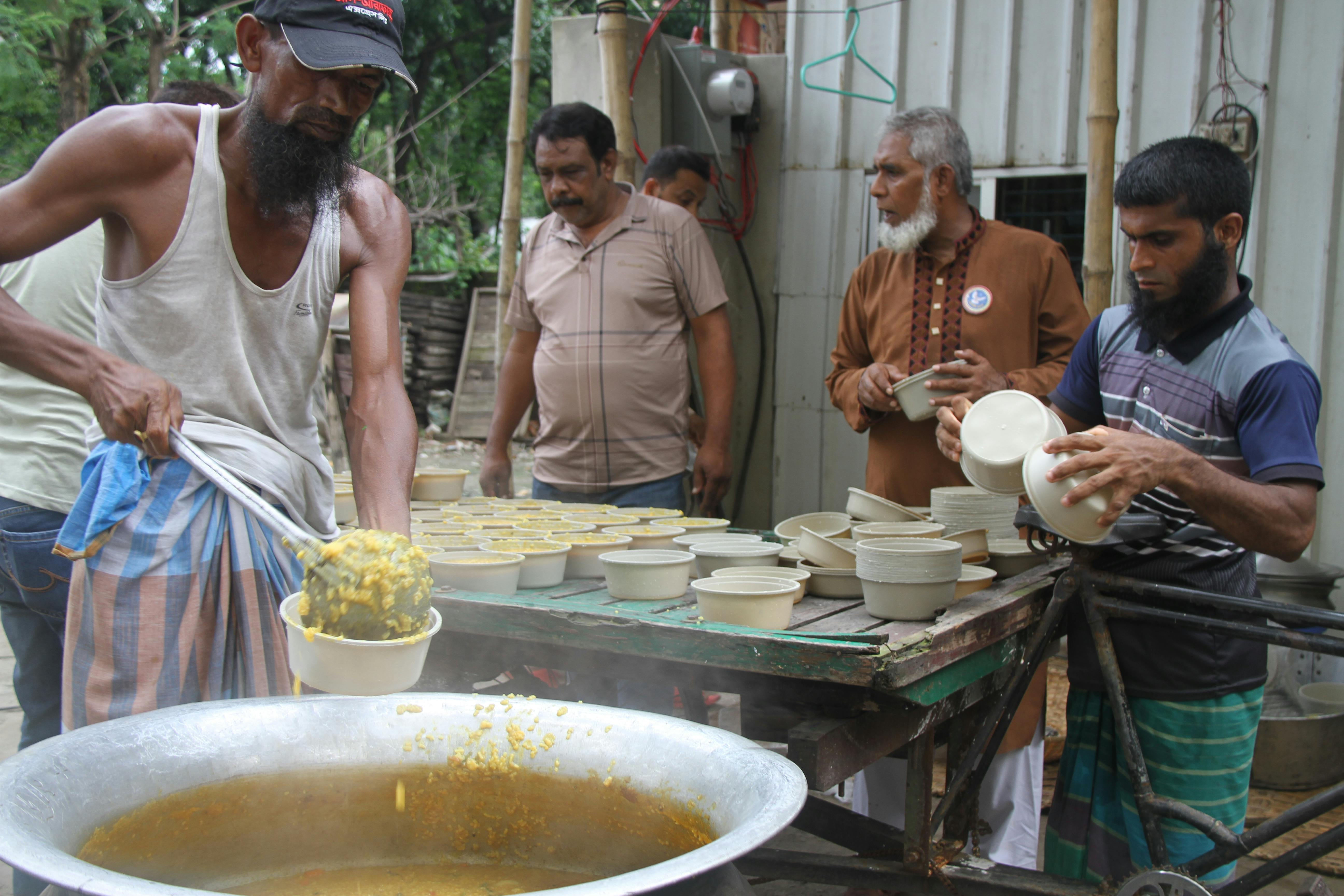 Men preparing and serving food in an outdoor setting in Keraniganj, Dhaka.