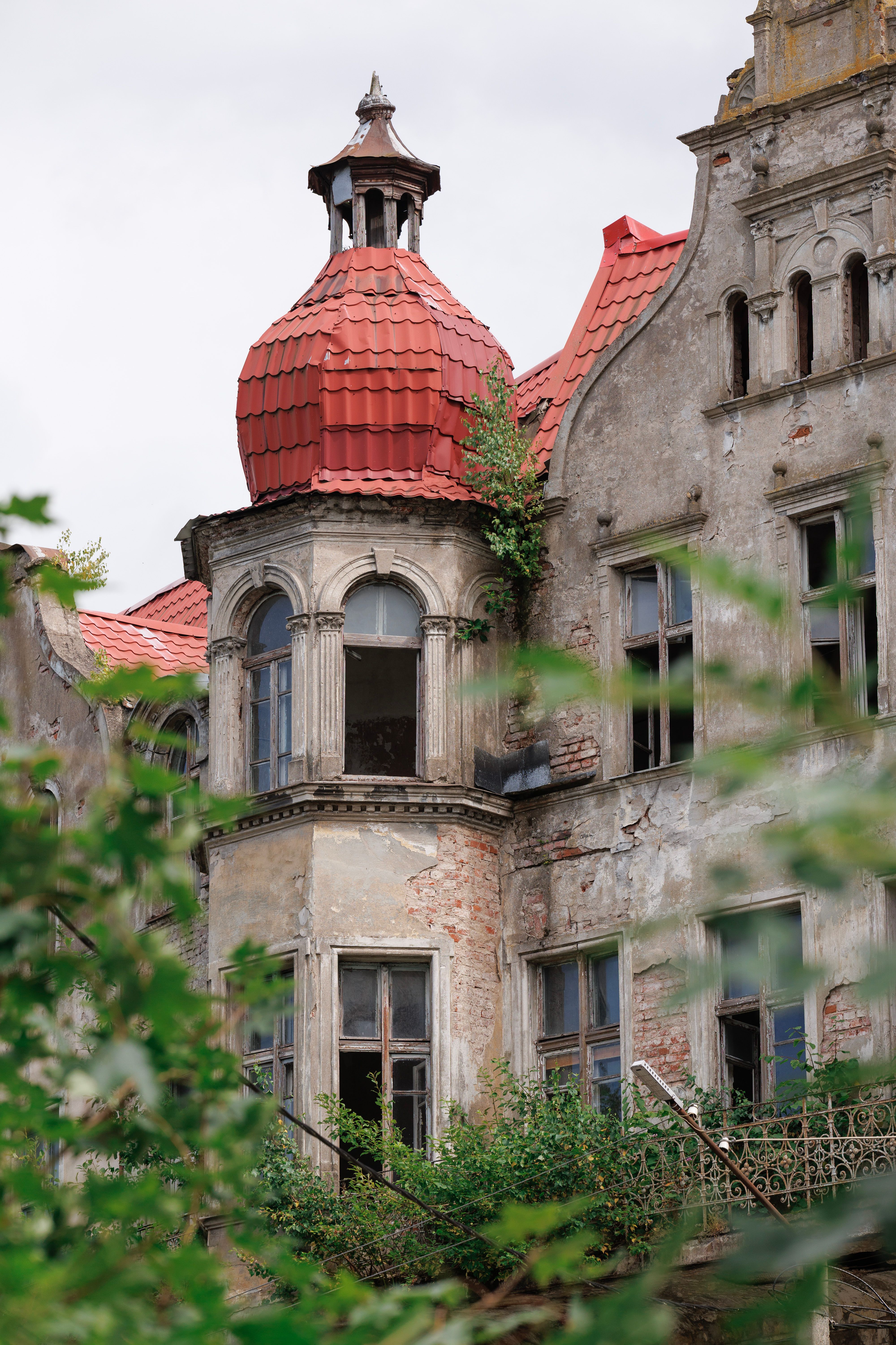 A close-up of an abandoned historic building with a distinctive red tiled roof and ornate architectural details.
