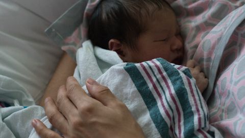 A peaceful scene of a mother cuddling her sleeping newborn in a hospital setting.