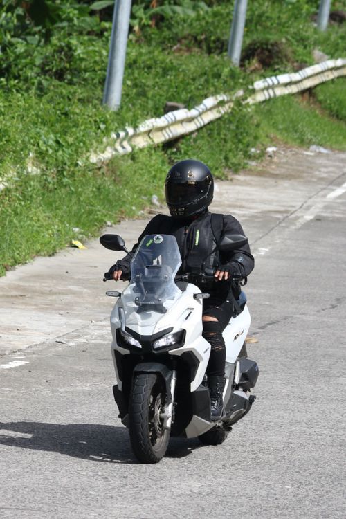 Free A motorcyclist rides a white scooter on a suburban road during the day, wearing full gear. Stock Photo