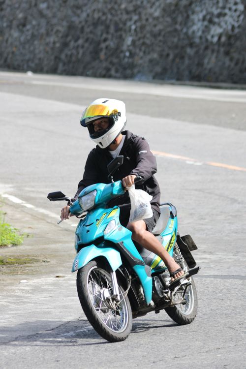 Free A man wearing a helmet rides a blue motorcycle on a city road during the day. Stock Photo