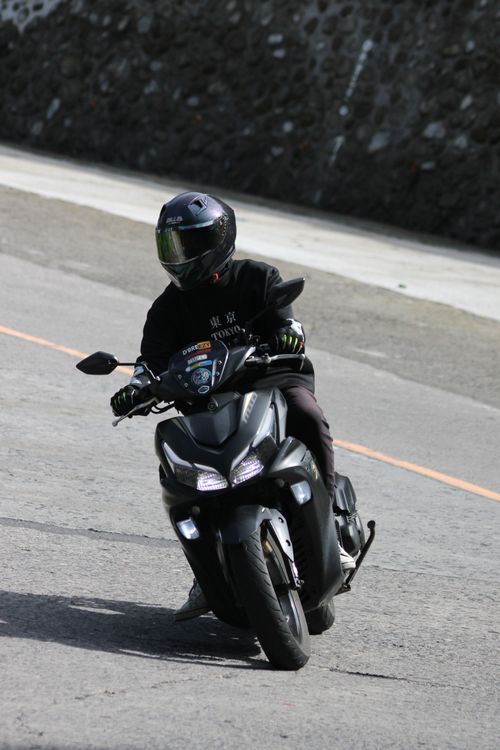 Free A motorcyclist wearing full gear rides a dark motorcycle down a road, embodying speed and safety. Stock Photo