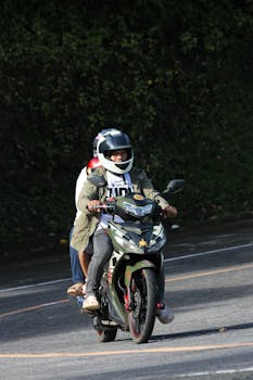 Two people on a motorcycle navigate a winding road surrounded by greenery.