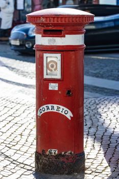 A classic red postbox on a sunlit cobblestone street in Olhão, Portugal, highlighting Portuguese culture.