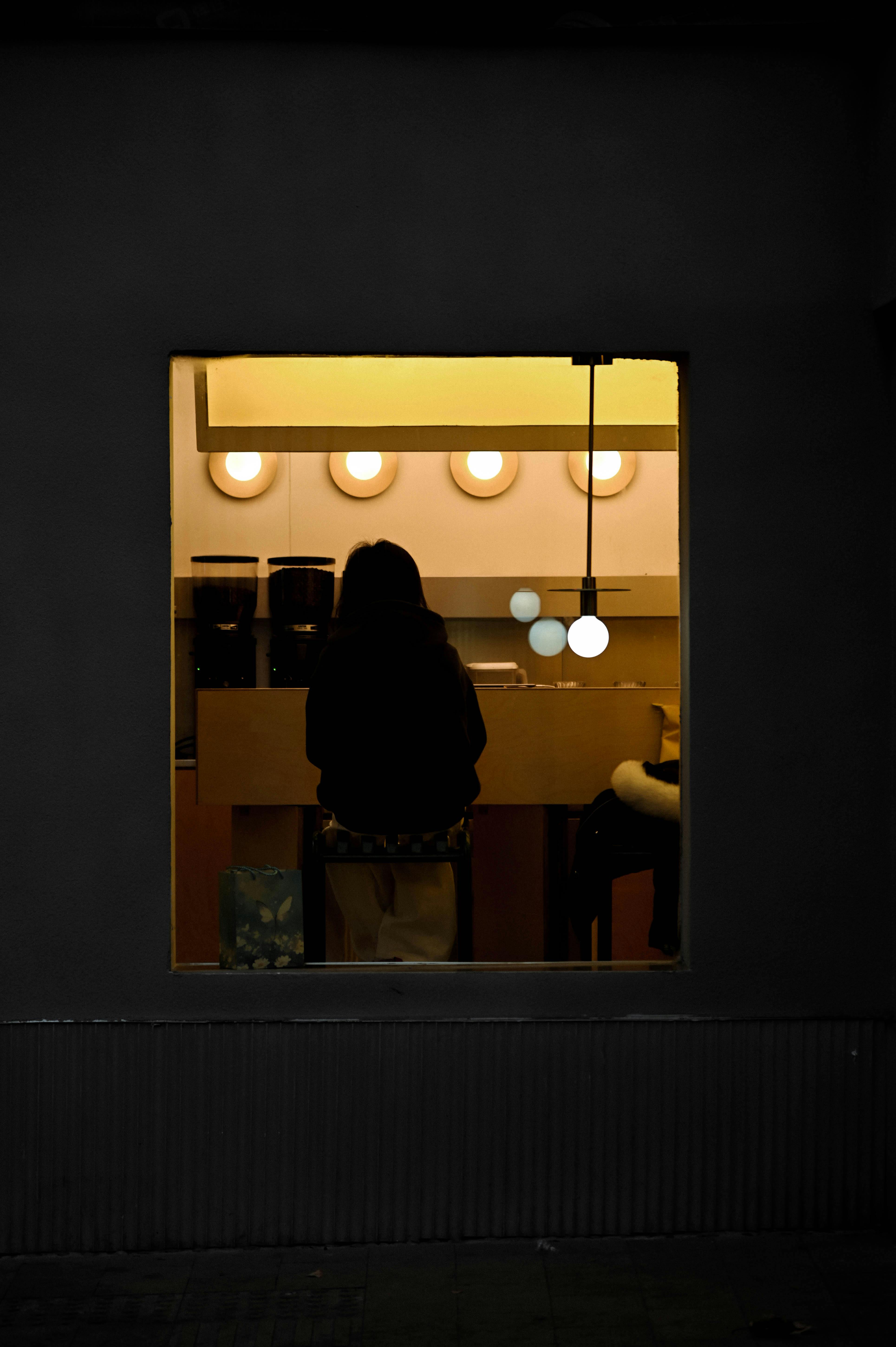 gratis Silhouet van een persoon die 's nachts in een schemerig verlichte koffiebar zit. Stockfoto