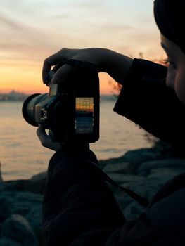 Silhouette of a person photographing a stunning sunset over the lake with a DSLR camera.