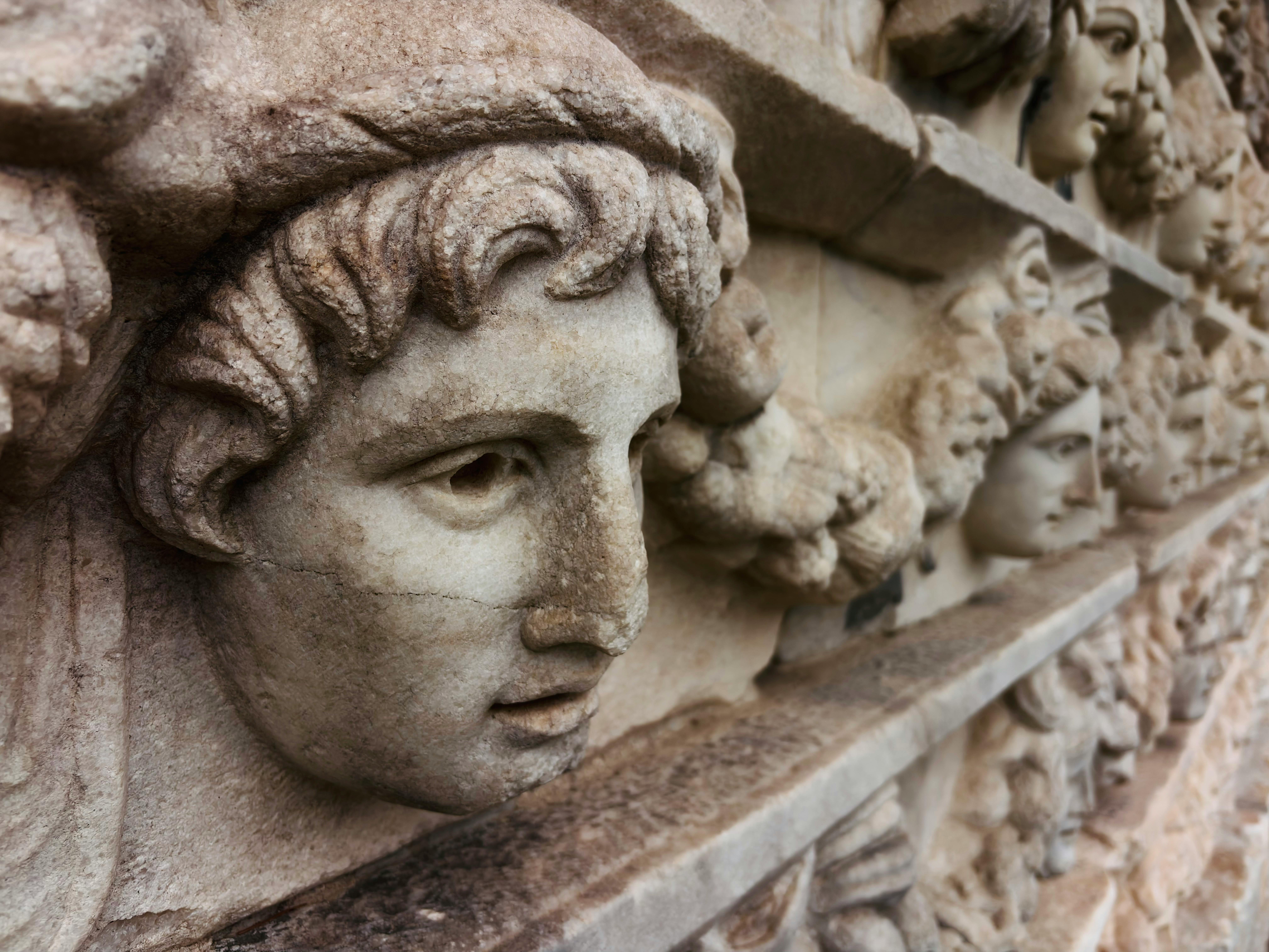 Close-up of ancient stone relief sculpture featuring detailed Greek faces.