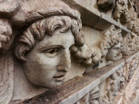 Close-up of ancient stone relief sculpture featuring detailed Greek faces.