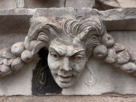 Close-up of a detailed stone gargoyle sculpture with an expressive face and intricate hair. Architectural detail.