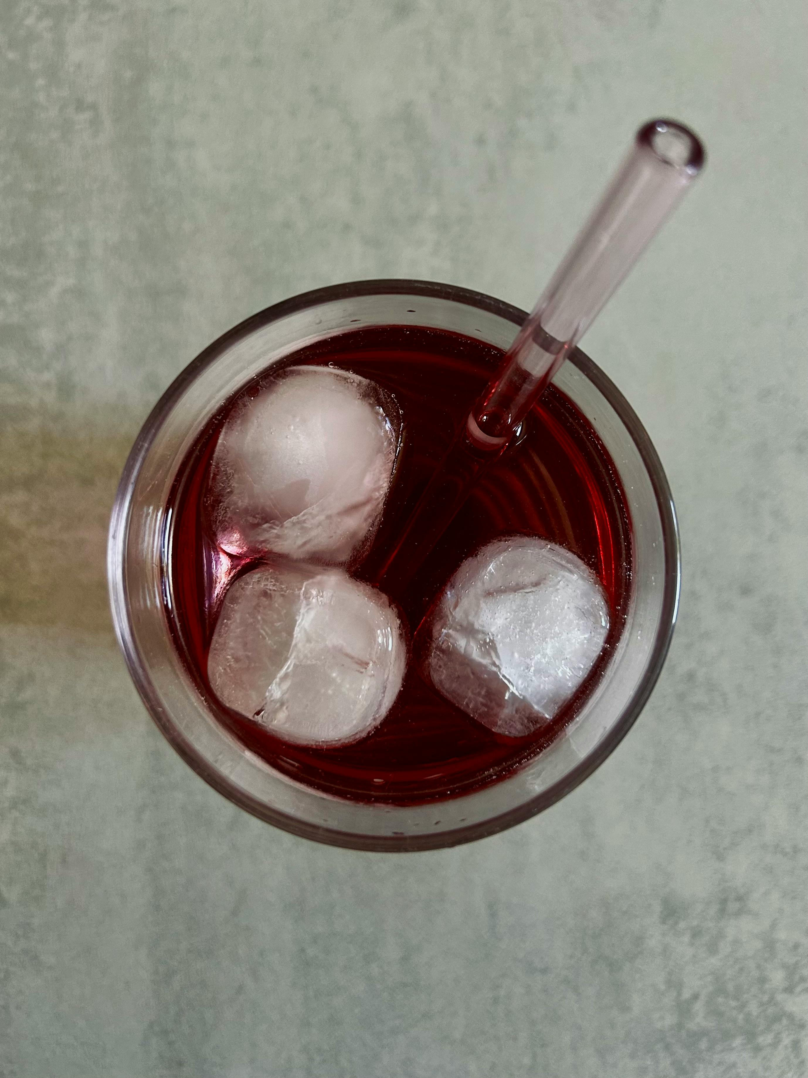 Overhead view of a berry drink with ice cubes in a glass, featuring a straw.