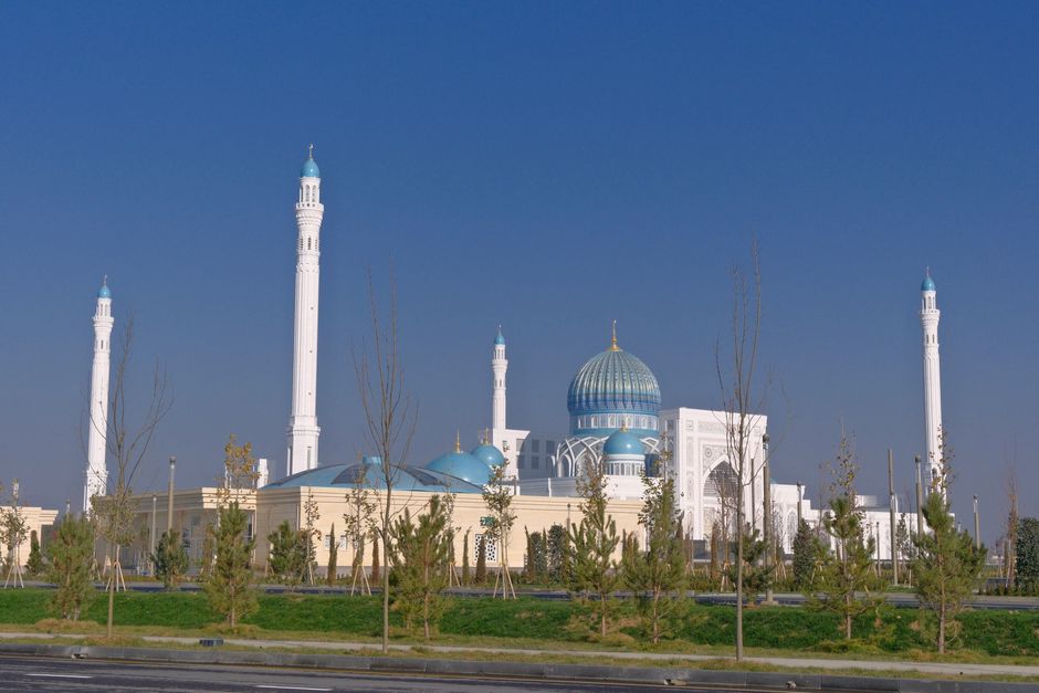 Beautiful mosque with blue domes and minarets against a clear blue sky, framed by trees.