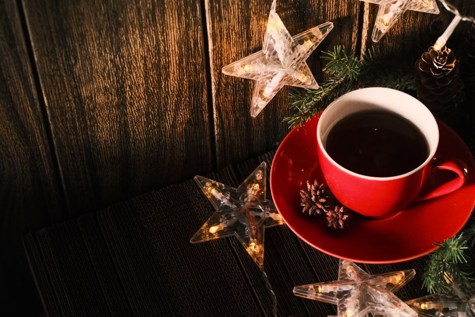 A warm, festive setup featuring a red cup of tea, pinecones, and star string lights on wood.