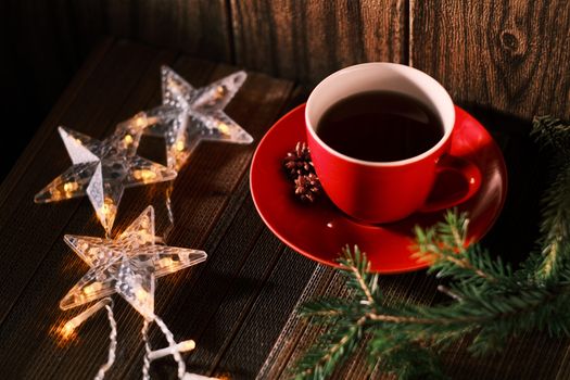 Warm festive setup with a red cup, star-shaped fairy lights, and pine branches.