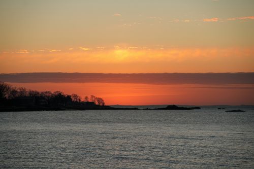 Free Peaceful sunset over the ocean with a silhouetted coastline and vibrant sky. Stock Photo