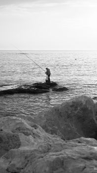 A lone fisherman on Byblos shore captured in a serene black and white setting.
