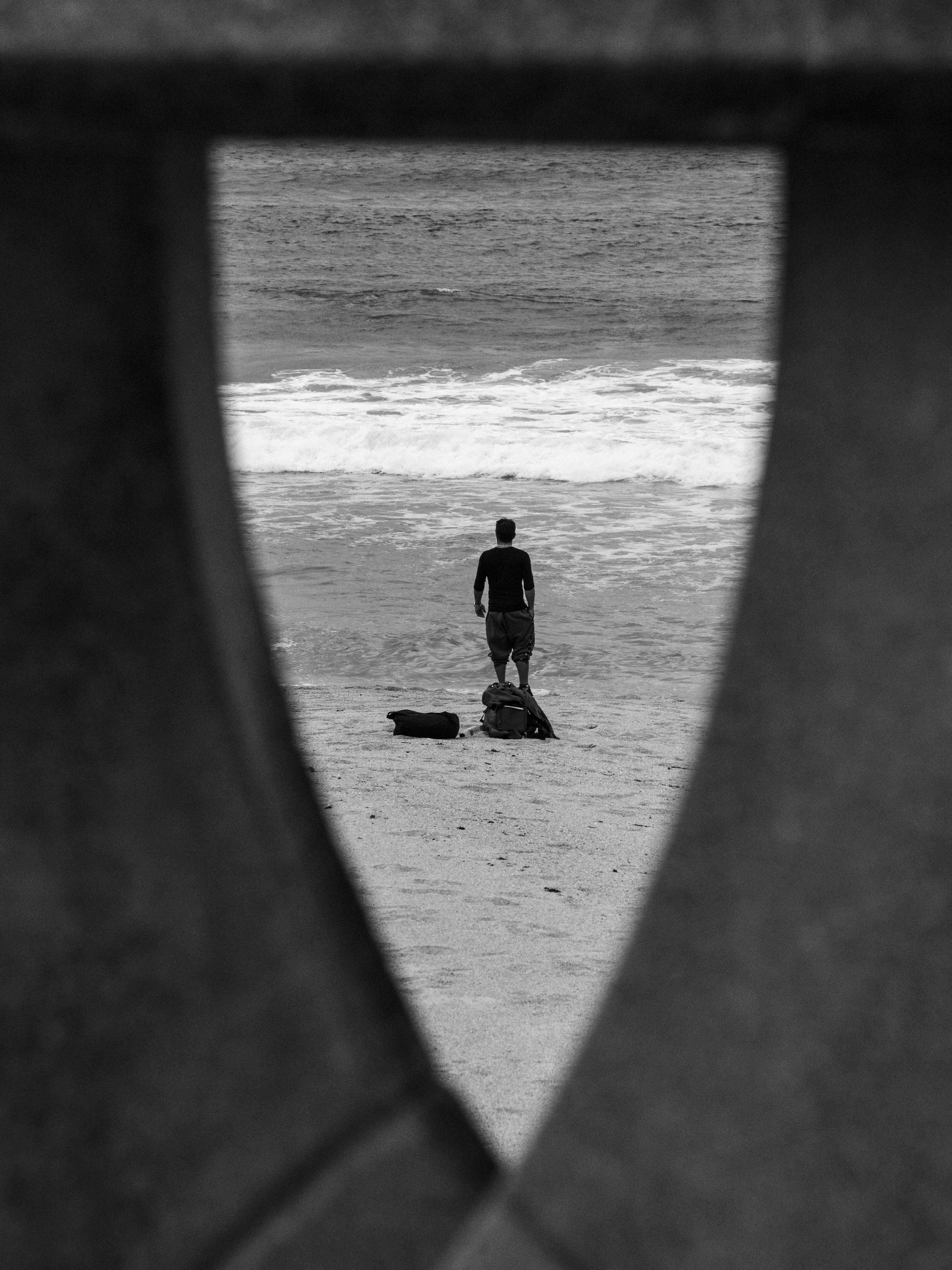 Gratis Una persona solitaria è in piedi su una spiaggia sabbiosa, visibile attraverso una ringhiera decorata. Foto a disposizione