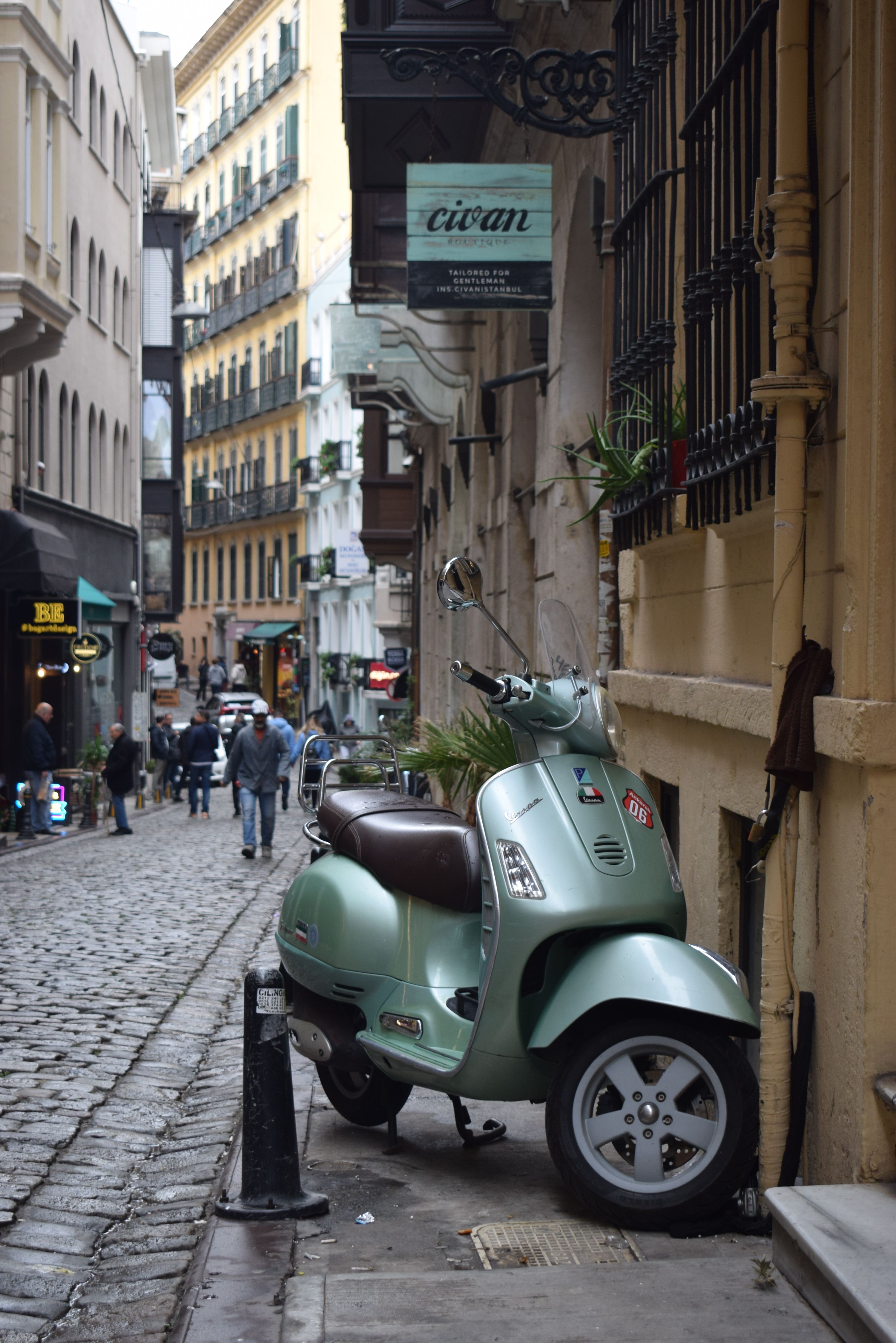 A classic scooter rests along a narrow cobblestone street in a historic European city.