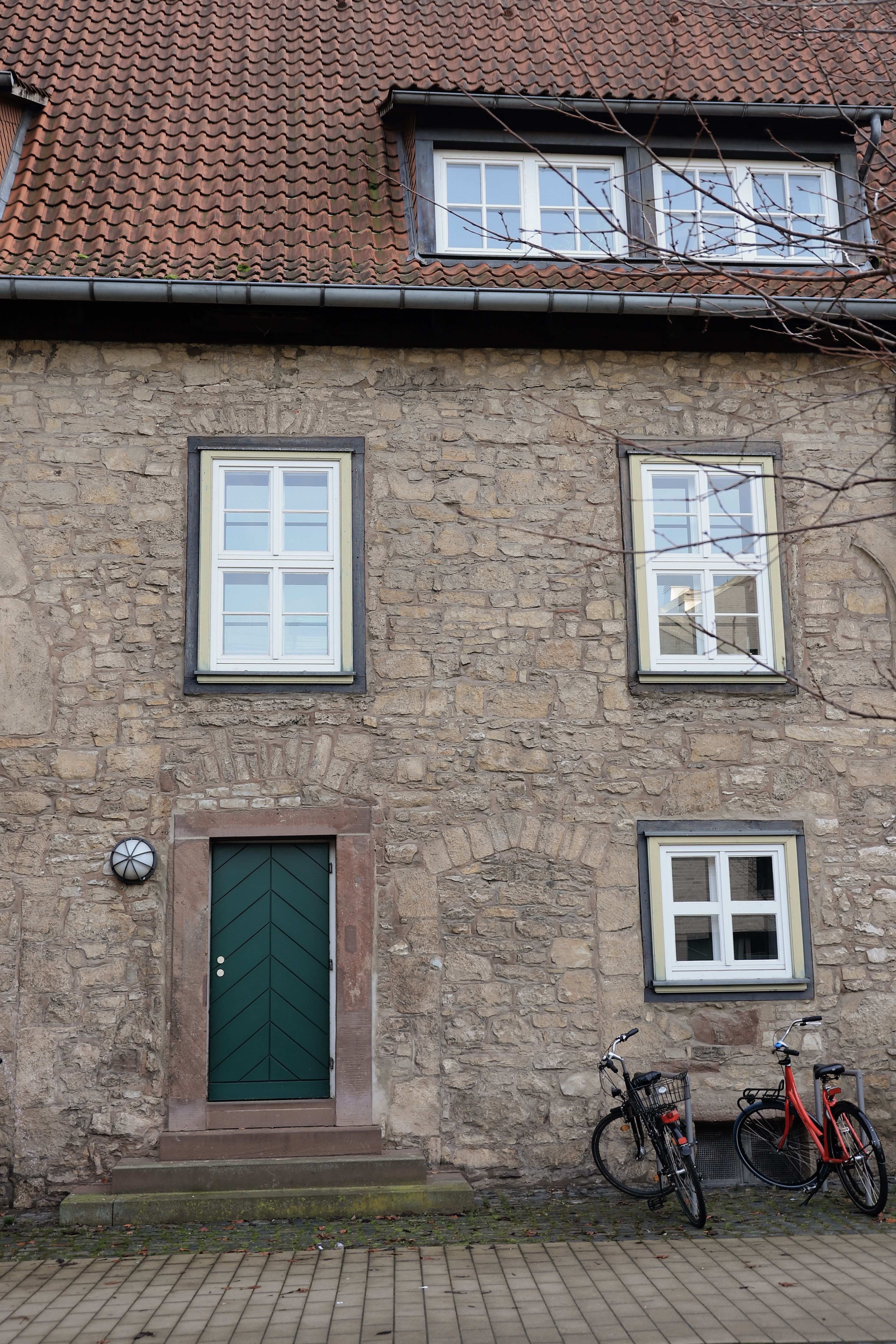 Façade en moellons de calcaire, fenêtres à petits carreaux et porte verte à encadrement de grès rouge.