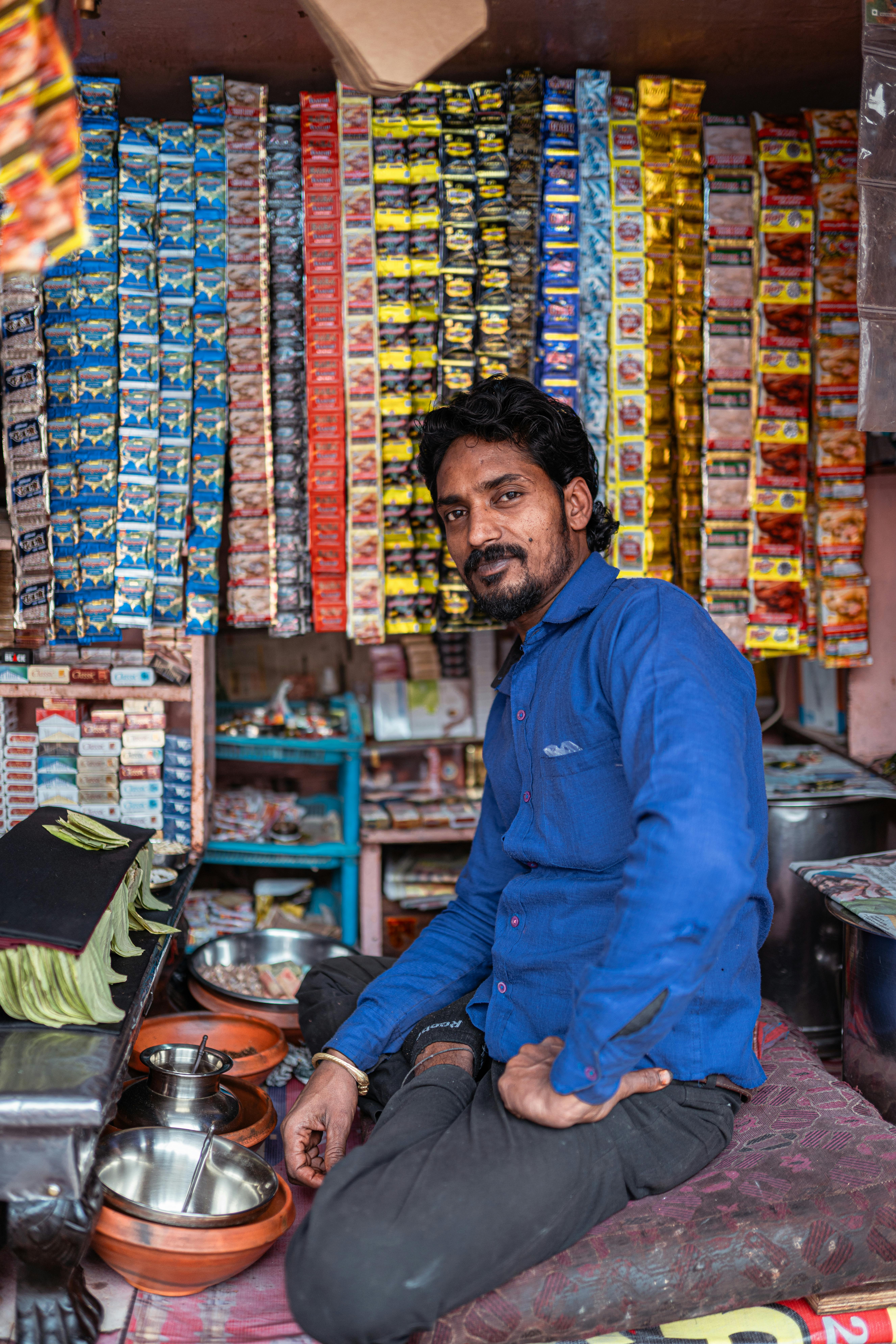 A street vendor in Varanasi, India, poses in his shop with colorful product displays.