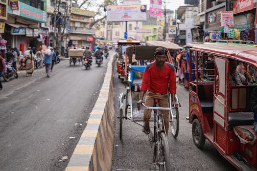 Bustling street in Varanasi with a man on a bicycle rickshaw and tuk tuks.
