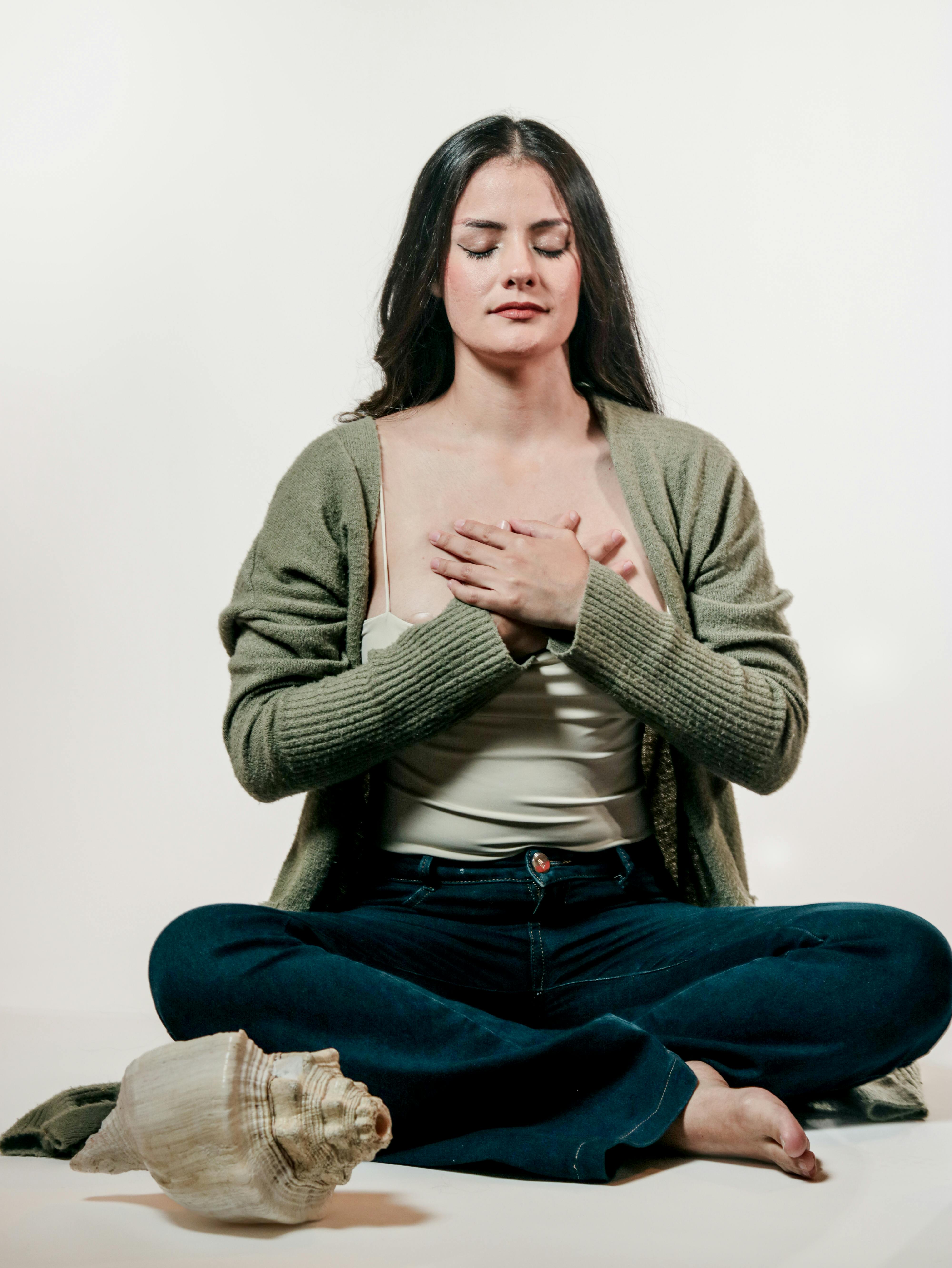 Woman meditating with closed eyes, hands on chest, and conch shell on the floor, invoking calmness.