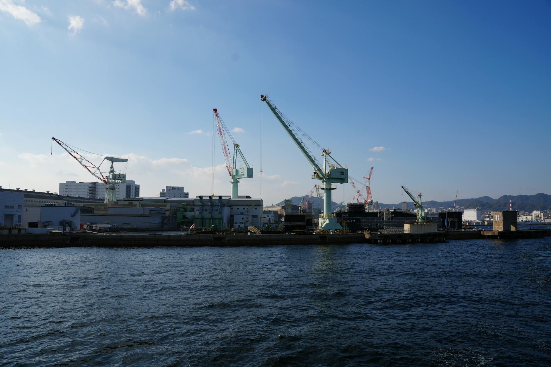 View of cranes at Kobe port under a clear blue sky, showcasing Japan's industrial capabilities.