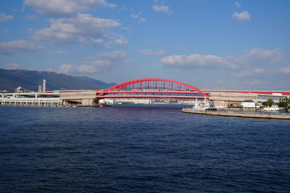 Bright red bridge over Kobe port under a clear autumn sky, showcasing modern architecture.